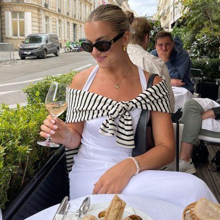 collage of influencer Izzy Dilger sitting at an outdoor cafe in Paris, France with. aglass of wine wearing a striped T-shirt over her shoulders and a white sleeveless dress