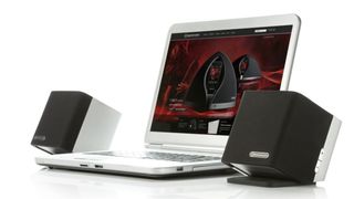 Some PC speakers on either side of a white laptop, on a white background. The laptop has some visualization of entirely different computer speakers on a red background. 