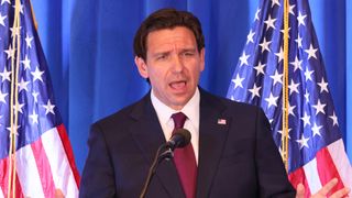 Florida Gov. and 2024 Republican presidential candidate Ron Desantis speaks at a lectern flanked by two American flags.