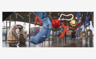 Wide view of Charles Jeffrey's 'The Come Up' exhibition featuring a variety of sculptures including brown, white and yellow arches, red and white spheres and a red silhouette of a body