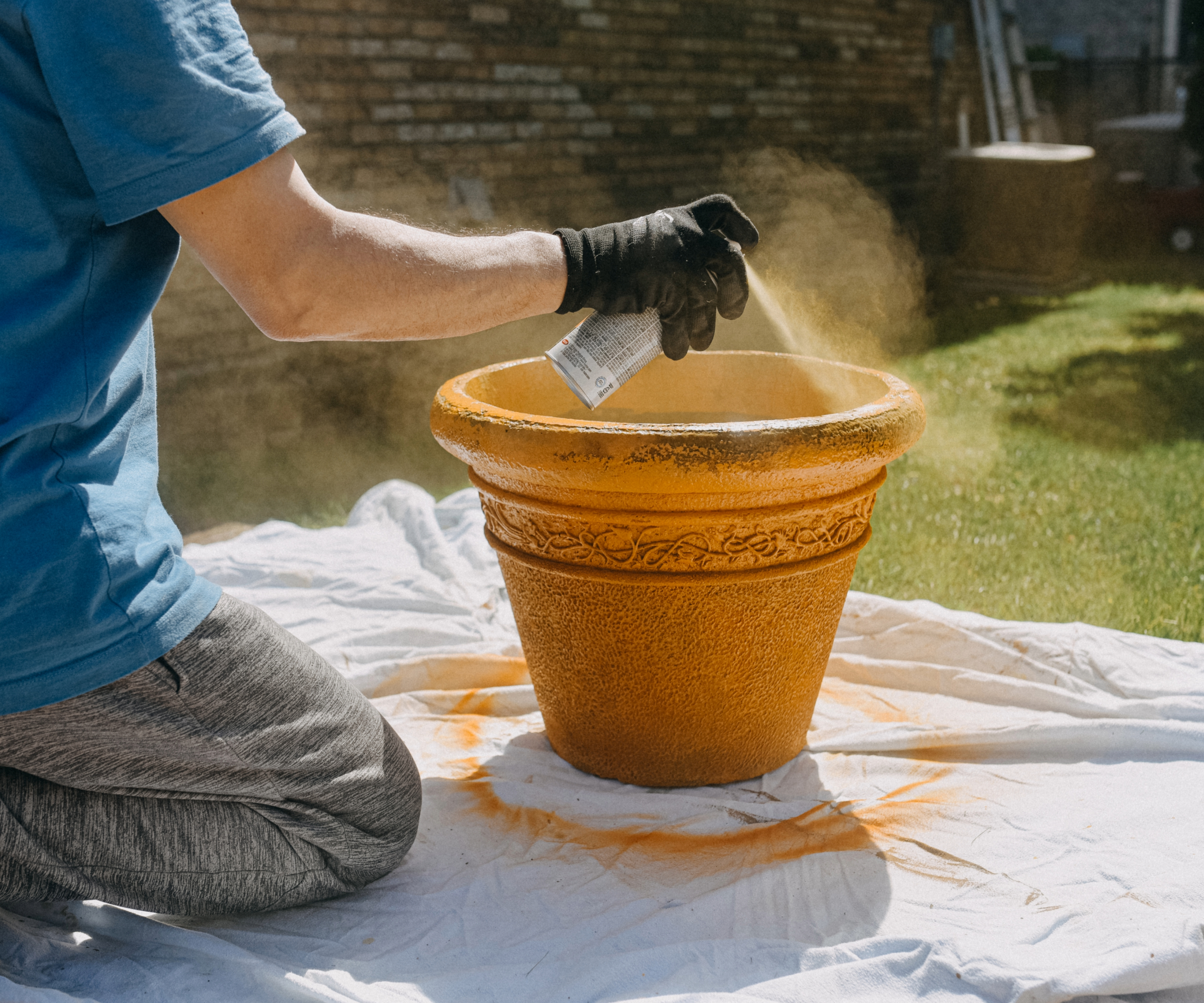 Person kneeling down while spray painting a pot yellow