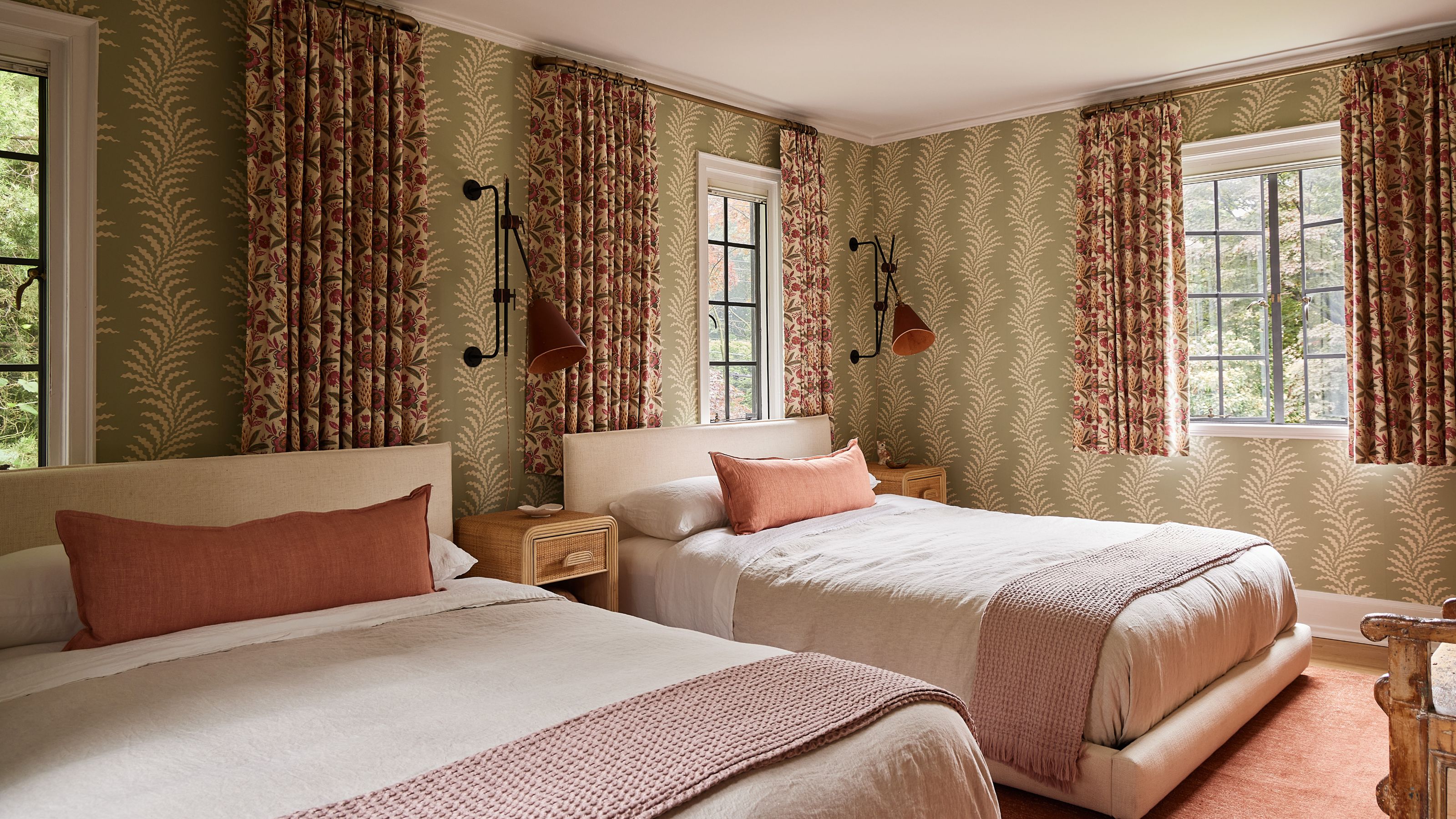 a layered guest bedroom with twin beds and green patterned wallpaper with floral pink tones curtains