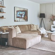 A neutral living room with a modern modular beige sofa with a mirror hung on the wall above it