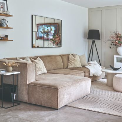 A neutral living room with a modern modular beige sofa with a mirror hung on the wall above it