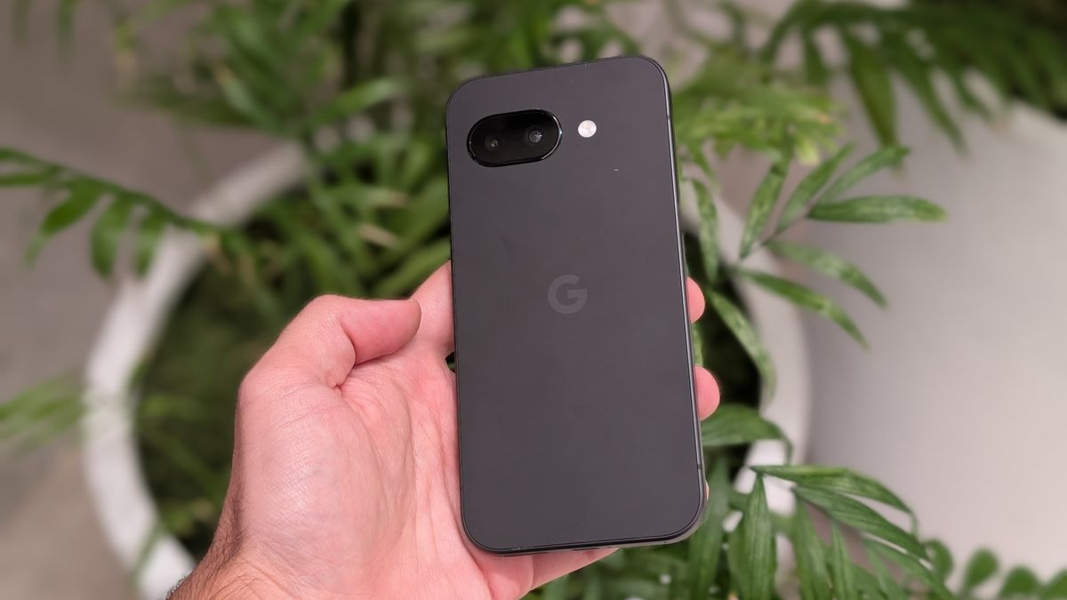 The Obsidian Google Pixel 9a held in hand above a houseplant.