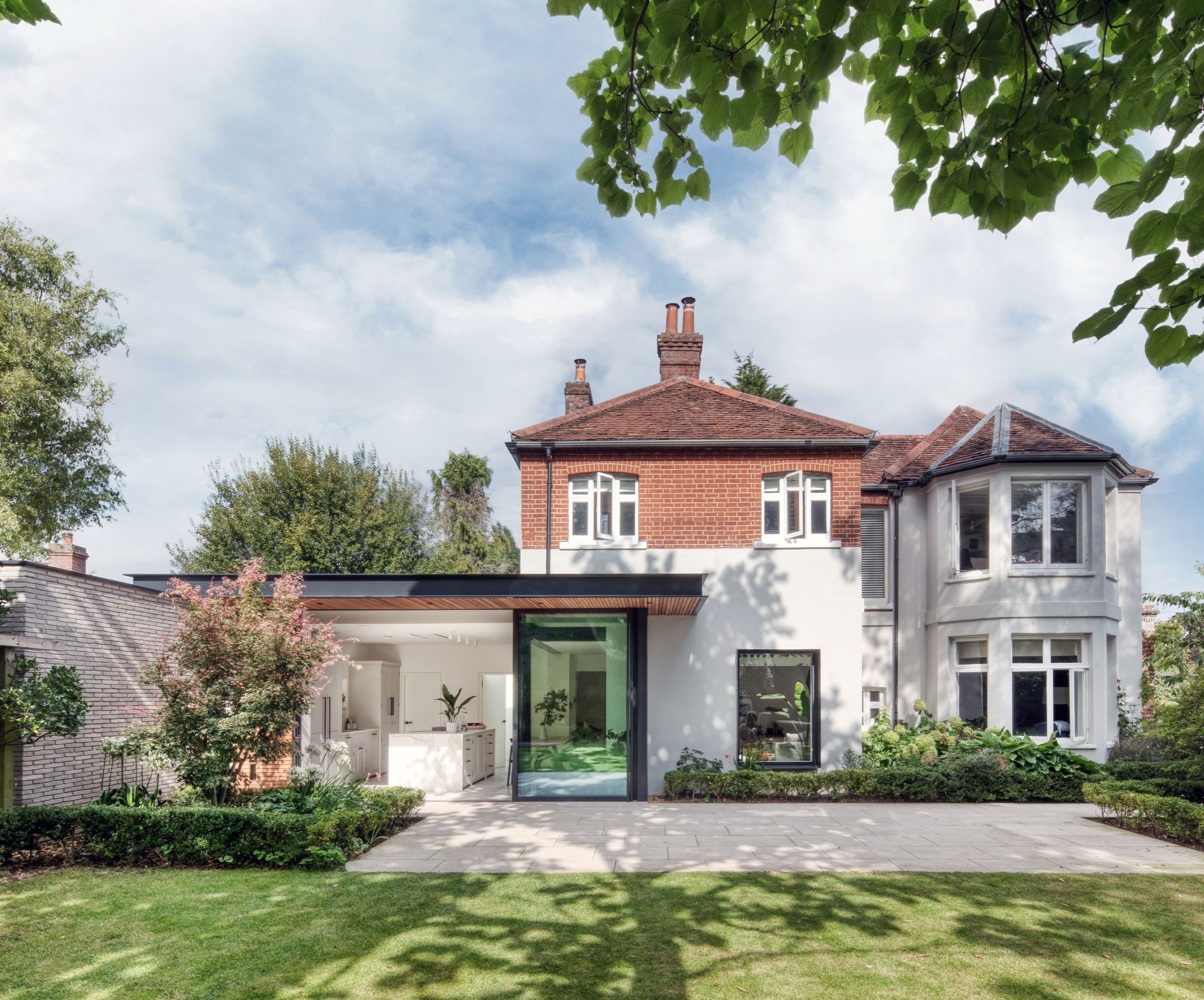 A redbrick home with white render on the lower storey and a large flat roofed extension with large bifolding glass doors out onto a patio and lawned garden