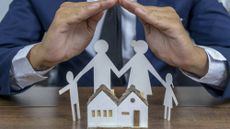 A man protecting a cardboard cutout family and house with his hands
