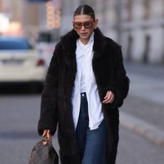 woman wearing a faux fur coat, a button down, and jeans