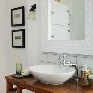 washbasin with wooden platform and white wall with white frame mirror