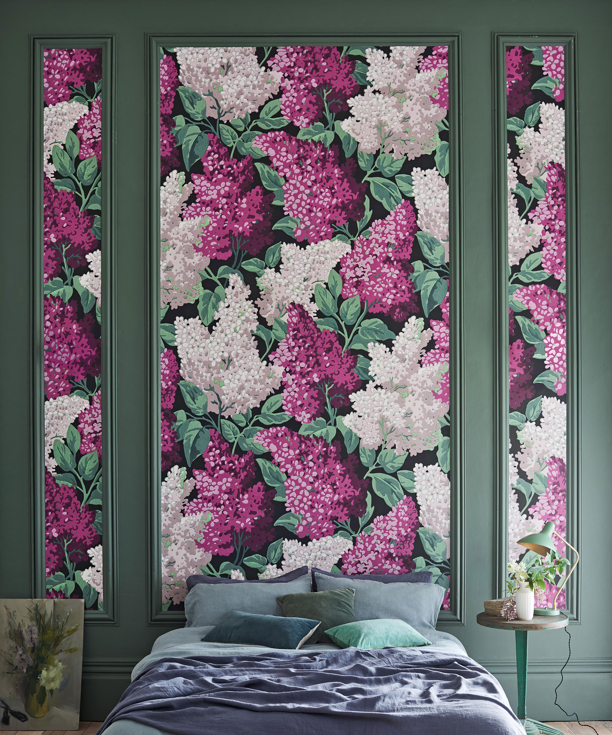 Pink and green botanical wallpaper broken up by green wall panels behind a blue bed