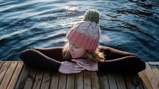 Woman wearing woolly hat in cold water pond, resting elbows against side