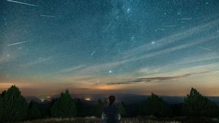 A man sits on top of a mountain watching the Perseid meteor shower