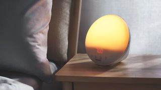 The image shows the Philips SmartSleep and Wake-Up Light on a bedside table in a dimly lit bedroom