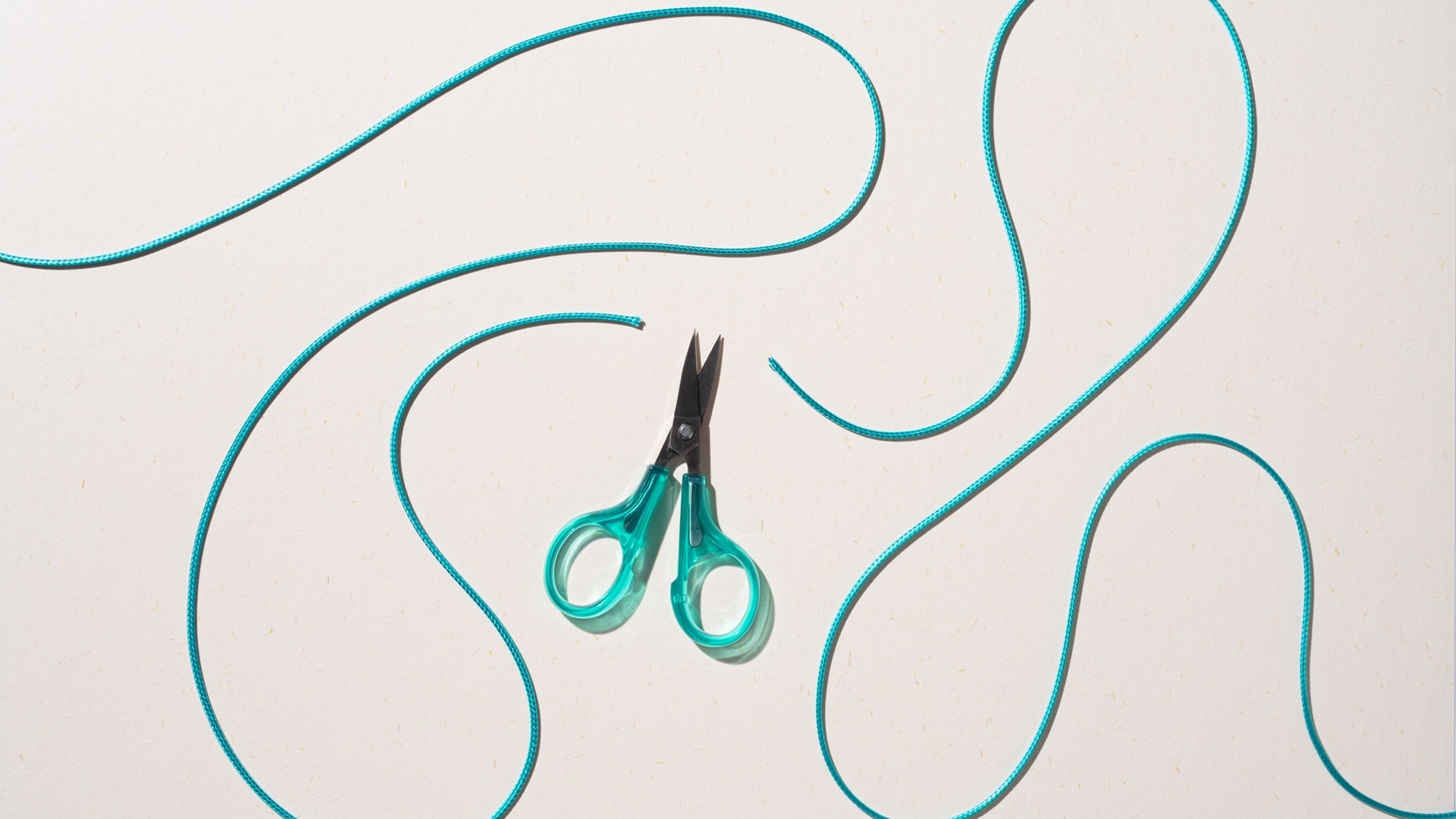 Scissors cut through a swirling green cord.