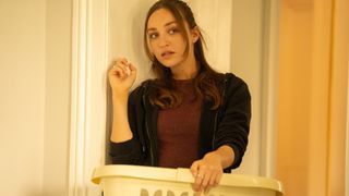 Ludmilla Makowski as Sandrine holds a washing basket and looks shifty in front of a door in The Au Pair.