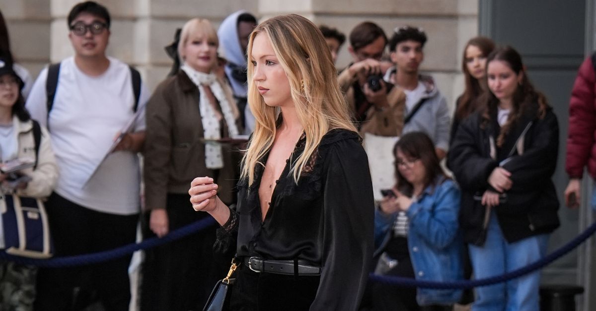 Lila Moss wears black flared jeans with a black blouse and heeled platform boots.