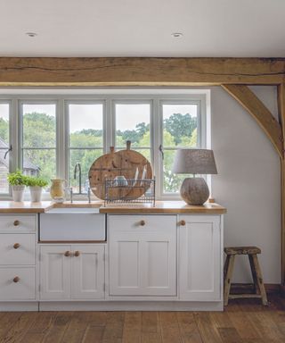 Kitchen with wooden floor and white units, wooden worktop and white walls with oak beams. A new build oak framed two bedroom house in the New Forest in Hampshire, home of Elizabeth and Derek Sandeman