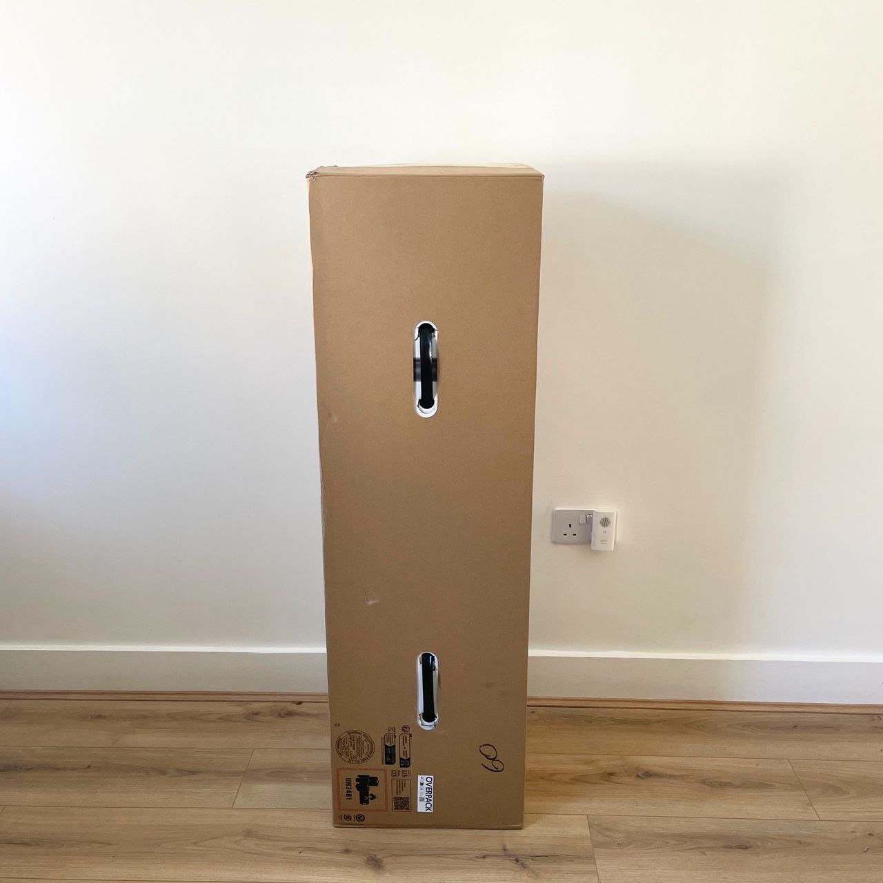 Dyson V10 Konical Cordless Vacuum and Auto-Empty Dok in a brown box, sitting on wood-effect flooring in front of a white wall