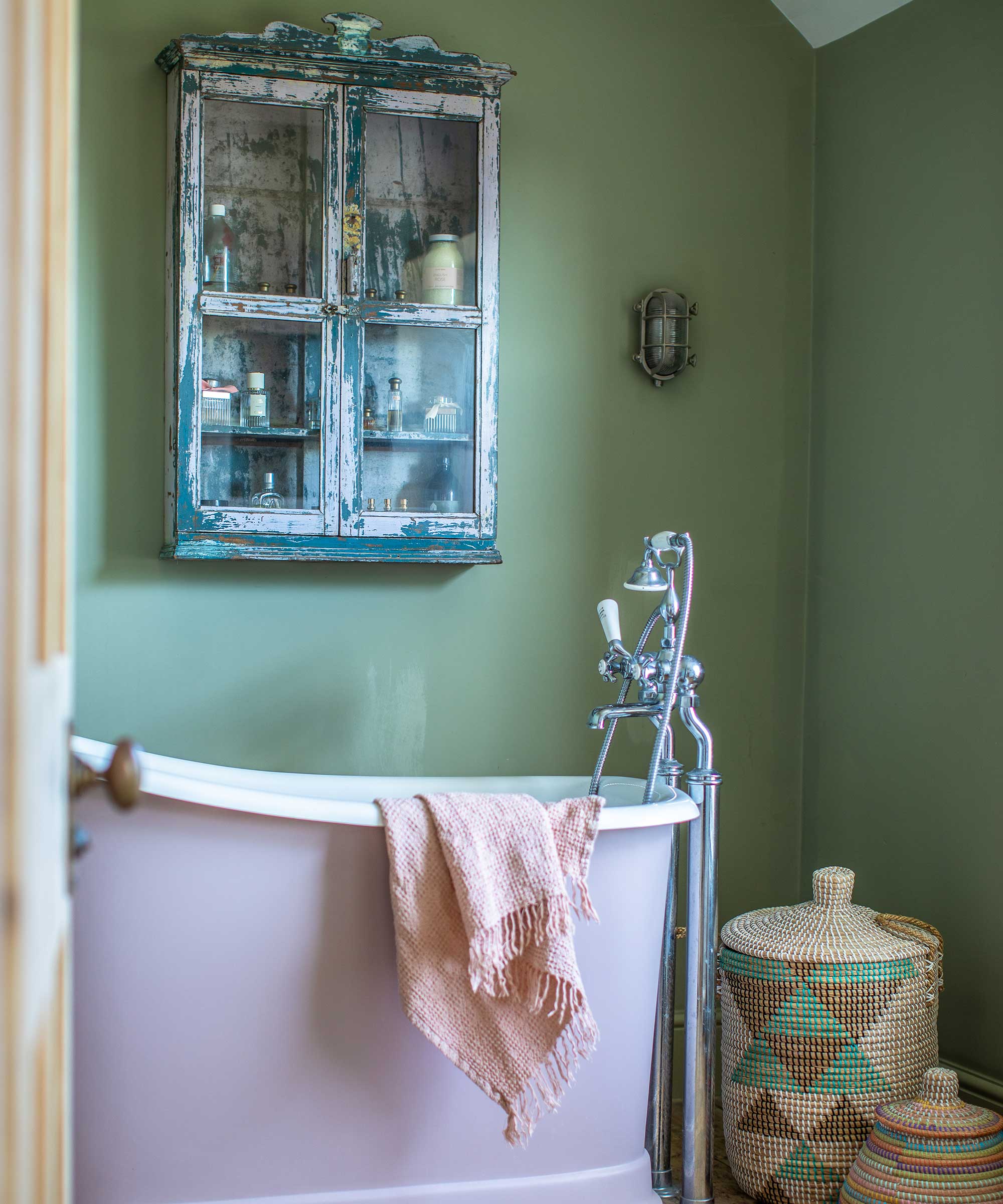 small green and pink bathroom with small roll-top bath, vintage wall cabinet, decorative laundry baskets