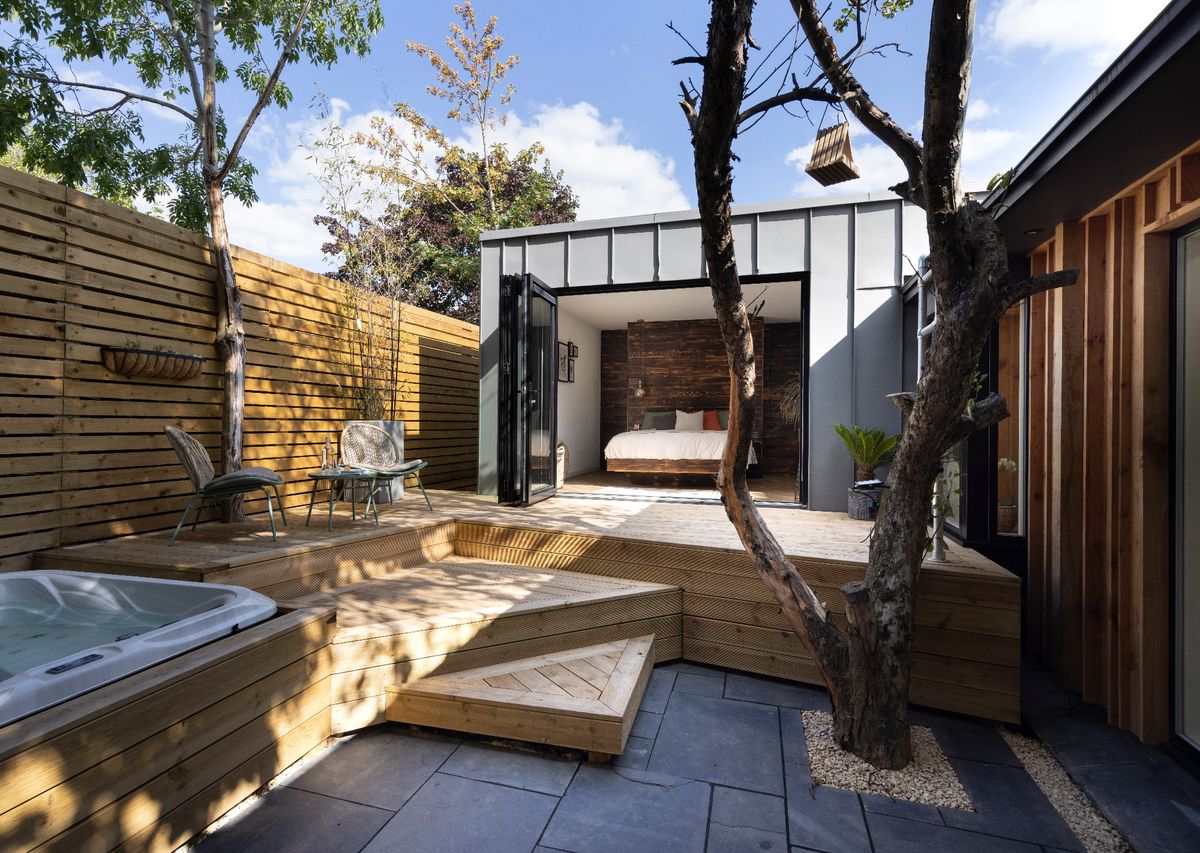 A small home with decking out the front, a sunken hot tub and steps leading down to a patio below