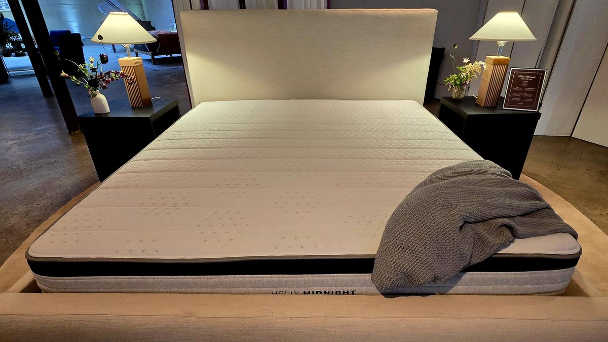 Helix Midnight Mattress 2025 on display with an upholstered platform bed frame with headboard, a gray throw draped over the bottom right edge