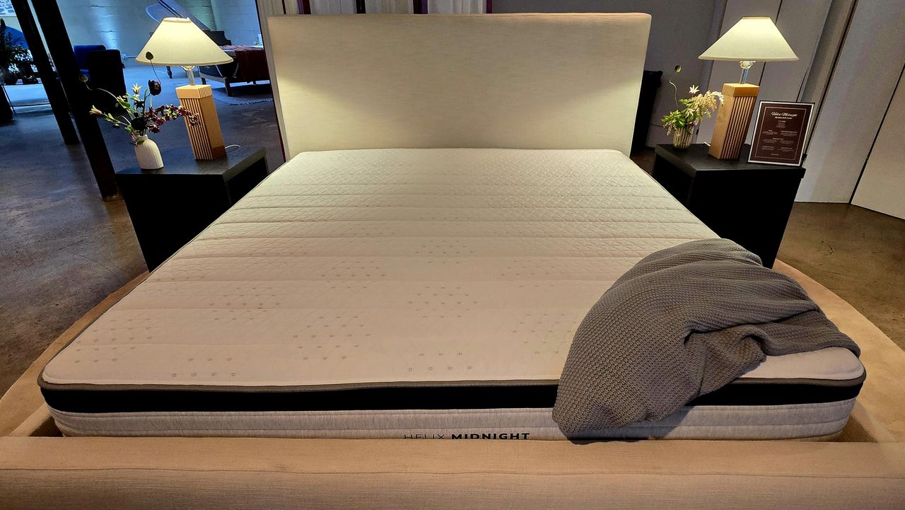 Helix Midnight Mattress 2025 on display with an upholstered platform bed frame with headboard, a gray throw draped over the bottom right edge