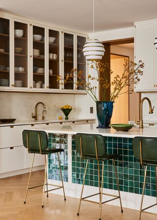 A view of a kitchen island covered in dark green tiles complete with three green stools