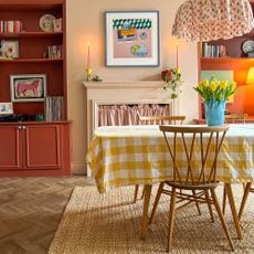 Dining room with parquet flooring, cream-peach walls and terracotta built-in shelving on either side of mantlepiece area