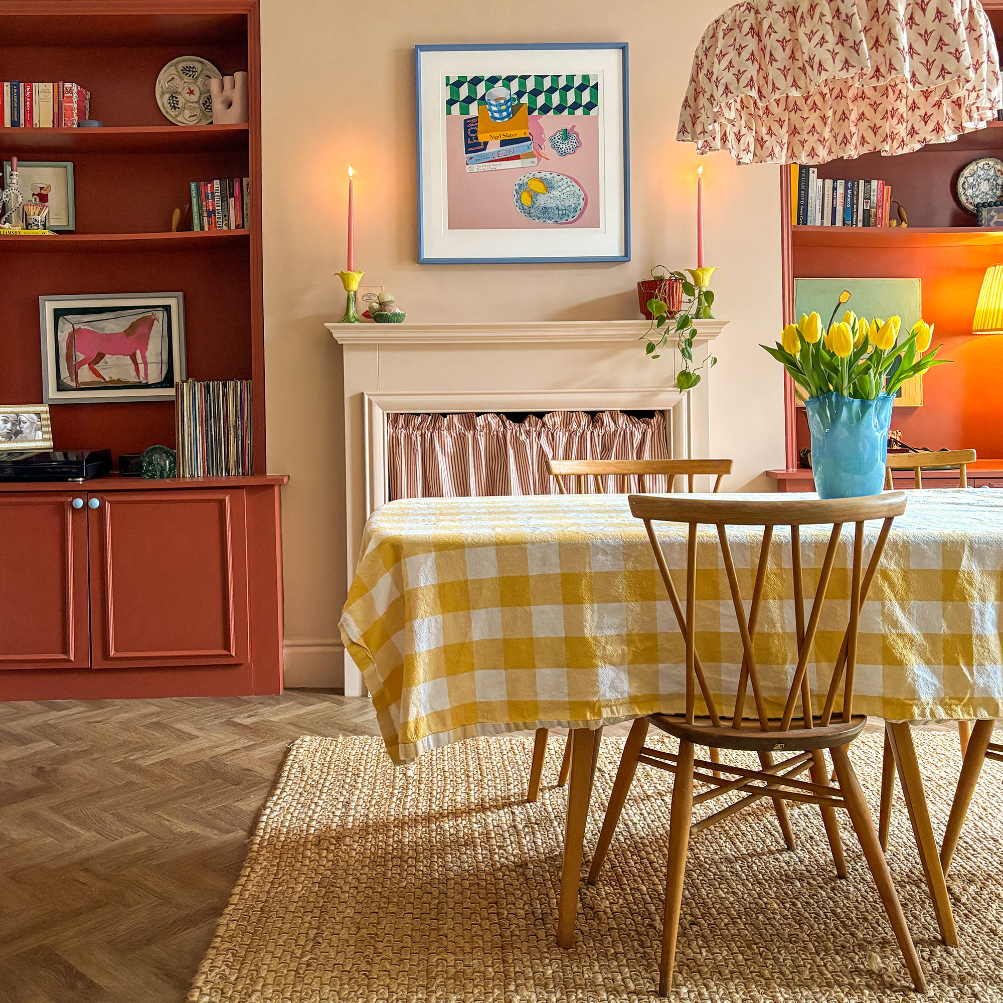 Dining room with parquet flooring, cream-peach walls and terracotta built-in shelving on either side of mantlepiece area