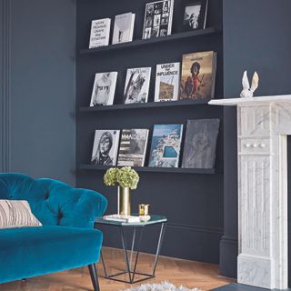 Living room with black walls, a velvet sofa, and books displayed on a built in shelf.