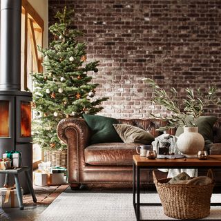 Living room with Christmas tree, log burner and leather Chesterfield sofa in front of exposed brick wall