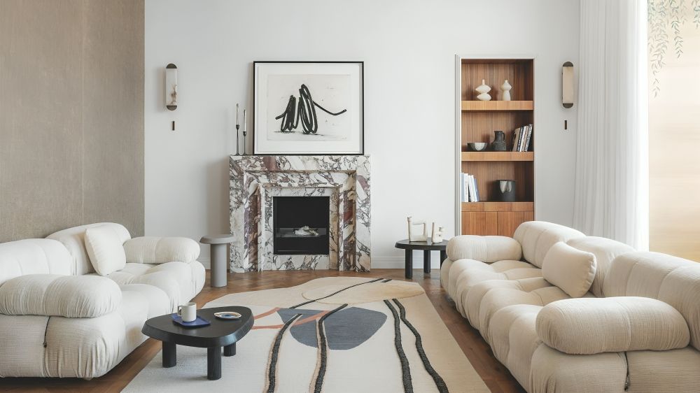 An open plan living area with parquet floor, fireplace with Calacatta Viola marble surround and off-white sofas.
