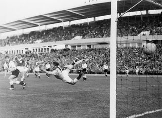 Northern Ireland's goalie, Harry Gregg, makes a graceful dive but misses the ball as West Germany's Uwe Seeler (not shown) scores during the World Cup soccer match. They tied the game at 2 points apiece. At left is Germany's Helmut Rahn