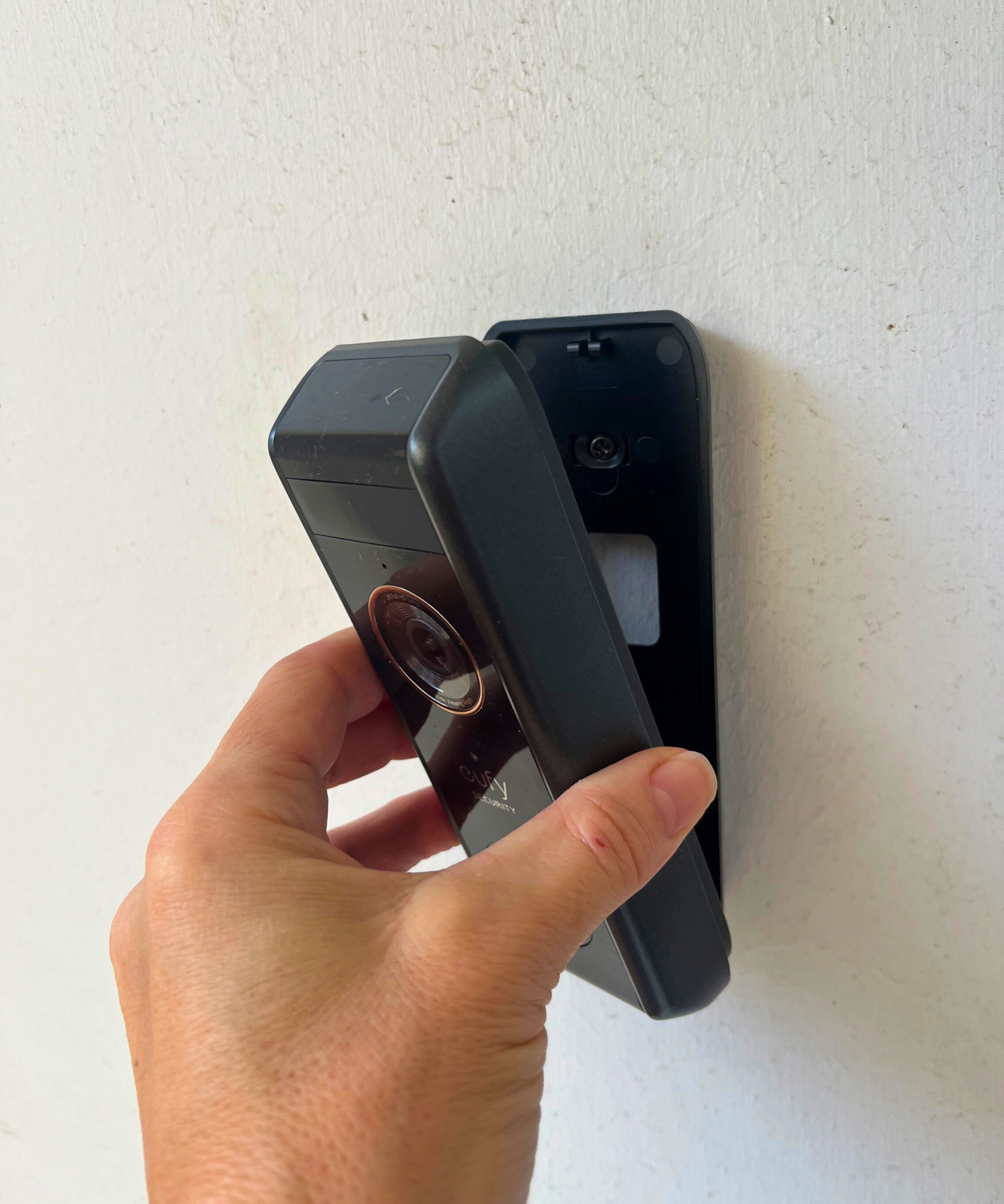 Hand positioning the eufy S330 video doorbell onto mount on white wall.