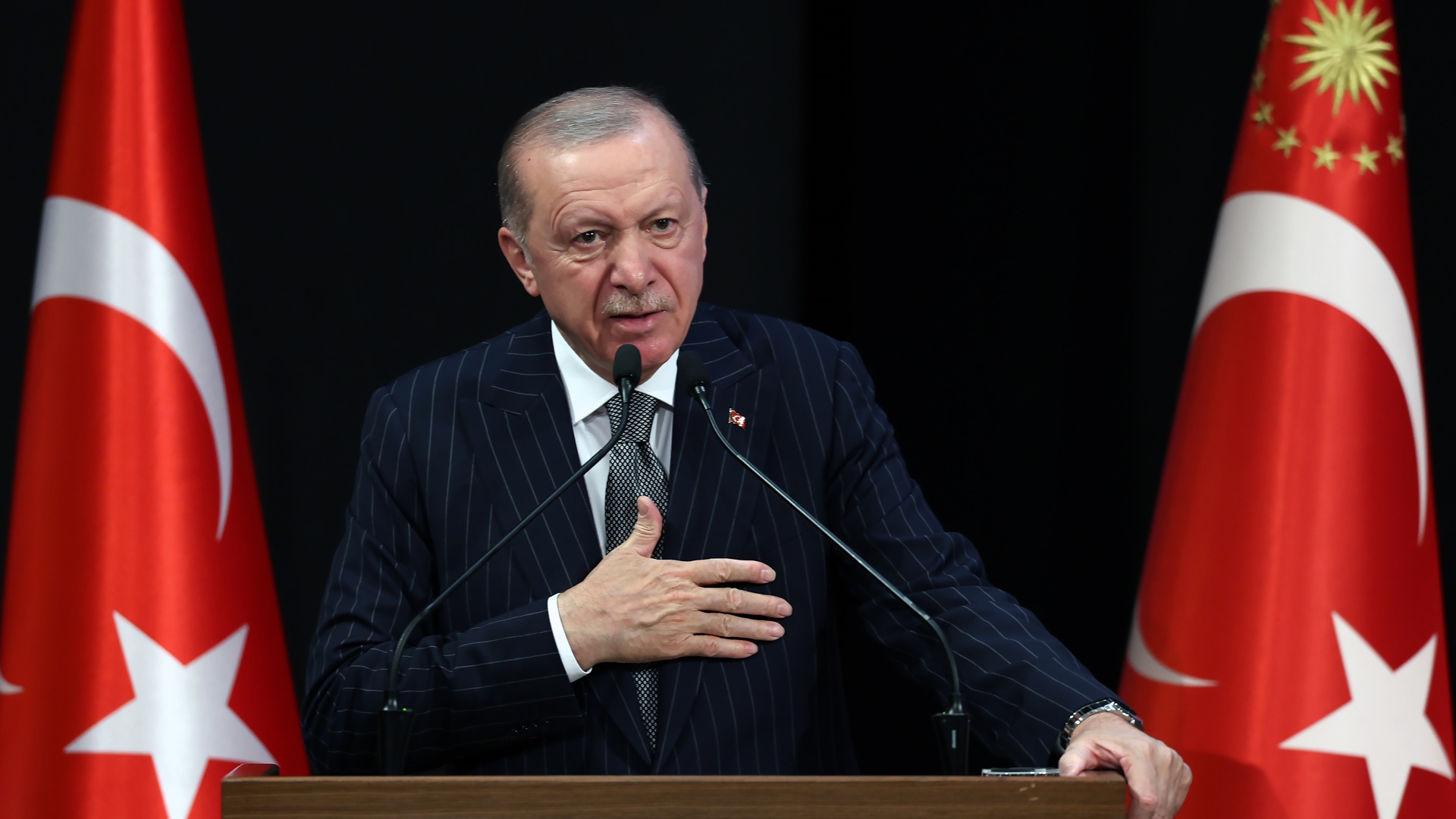 Turkish President Recep Tayyip Erdogan making a speech at a lectern flanked by two Turkey flags.