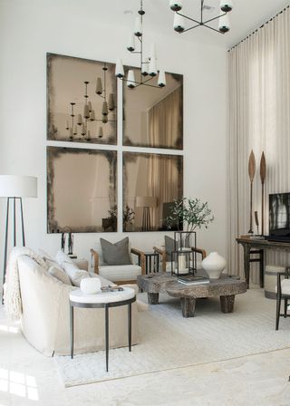 Wall of acid wash mirrors behind white and wooden armchairs in modern living room with stone coffee table