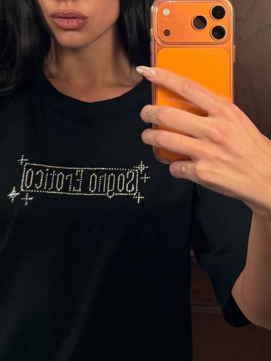 Dua Lipa taking a selfie in the mirror wearing a black T-shirt with her gold and silver starry manicure