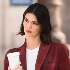 Kendall Jenner wears blue jeans, affordable loafers, red wine velvet jacket and a white tee as she carries a coffee cup