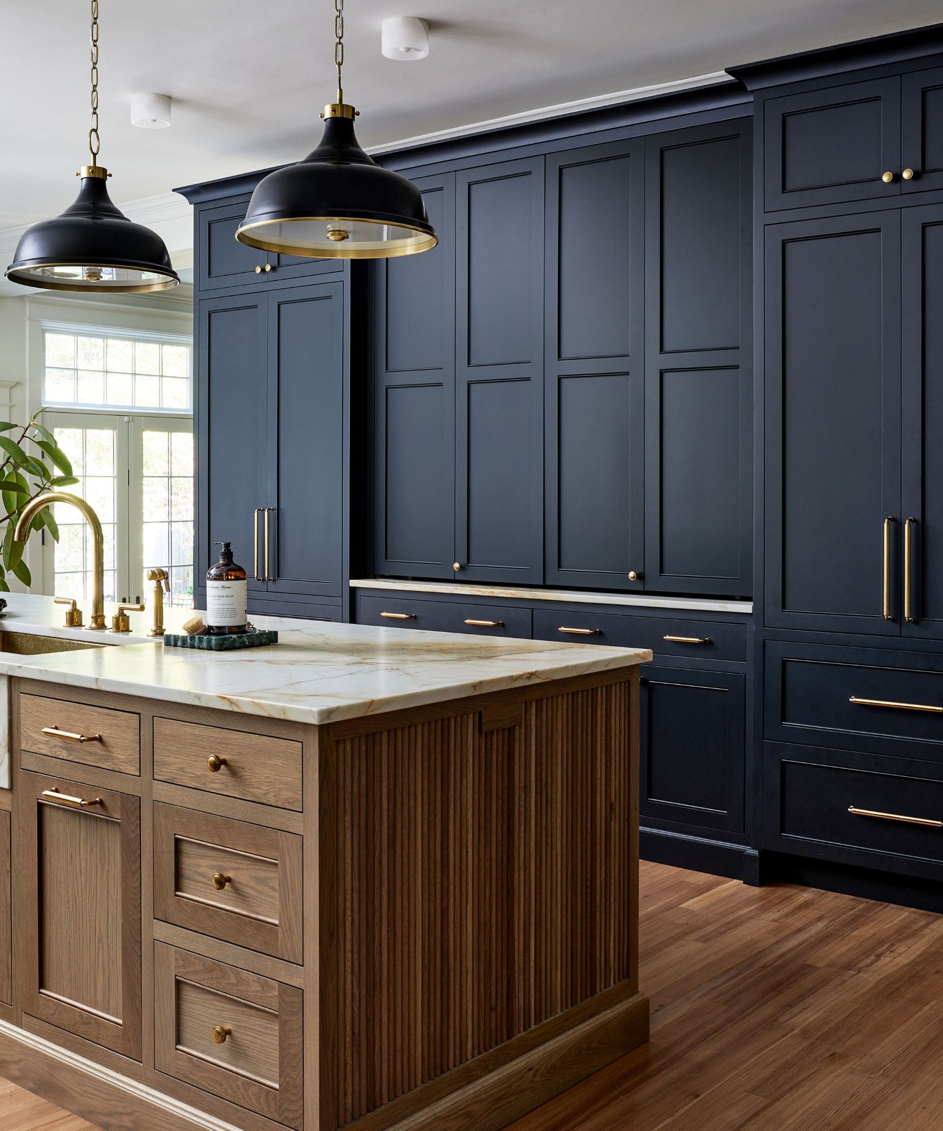 A kitchen with dark blue cabinets, brass hardware, and a wooden kitchen island