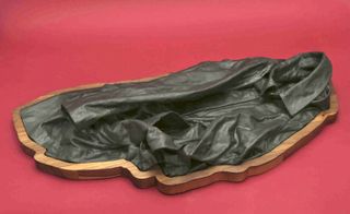 A black leather jacket displayed on an oddly shaped wooden base on a red surface.