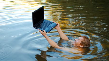 A man submerged in water holding a laptop above the surface.