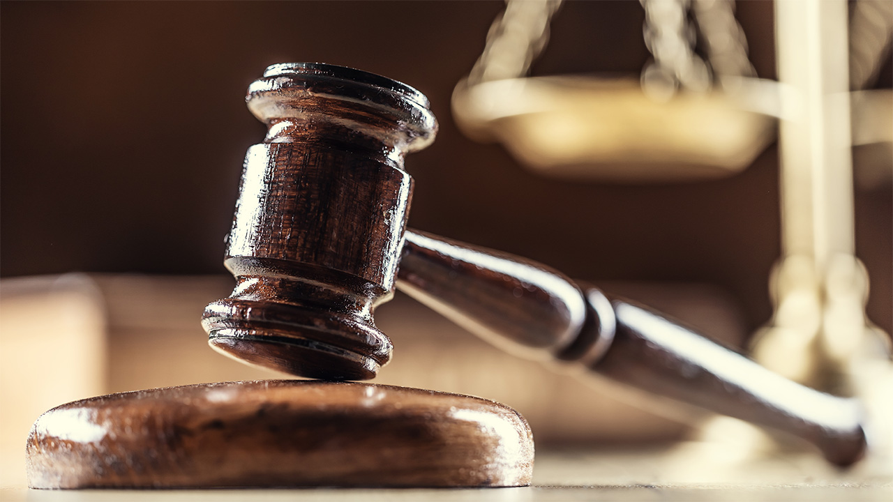 Judge's gavel resting on table, with scales and a legal book in the background