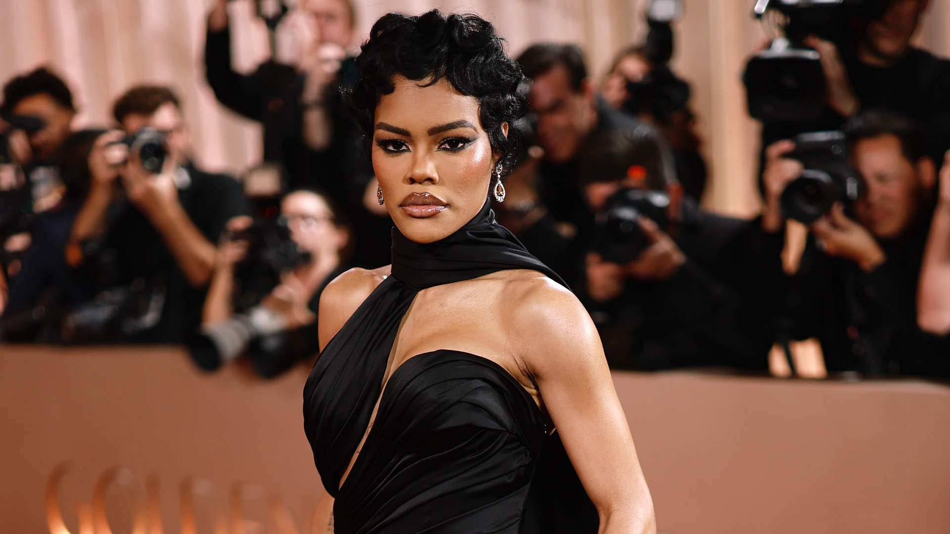 Teyana Taylor at the Golden Globes red carpet. She is wearing a black gown, a pixie hairstyle, and edgy eye makeup.