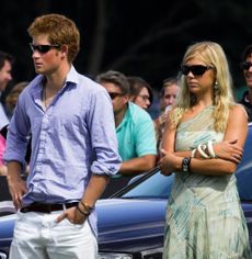 Prince Harry wearing a blue shirt standing next to Chelsy Davy, wearing a green dress