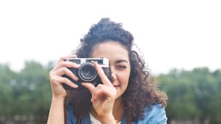 The best camera for beginners: a woman with curly hair holds a camera up to her right eye