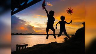 Two children jump silhouetted against a sunset in Myanmar