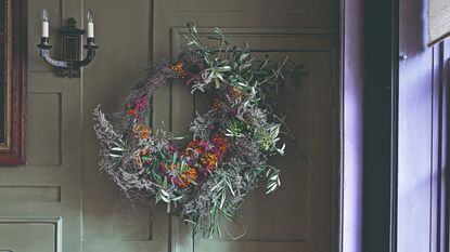 A room with wall panelling in sage green decorated with a large Christmas wreath hung on the wall