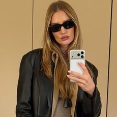 Rosie wears black sunglasses, a black leather jacket, and a pendant necklace.