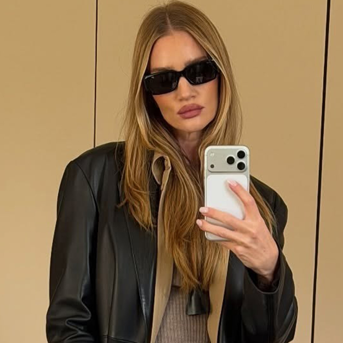 Rosie wears black sunglasses, a black leather jacket, and a pendant necklace.