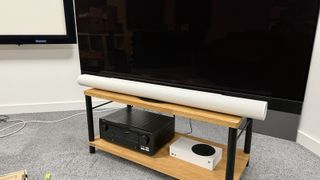 The Sonos Arc Ultra soundbar photographed on a wooden rack in front of a Panasonic OLED TV